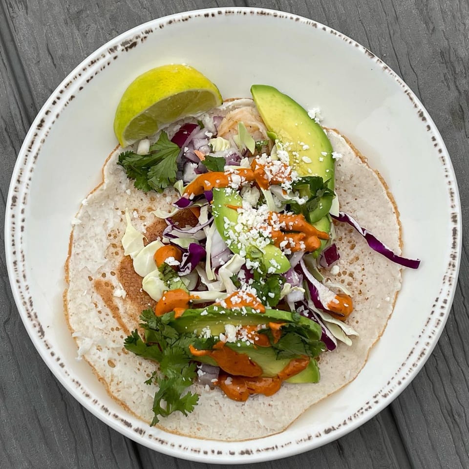 A Gorkha Palace Indian Cuisine taco with avocado, cabbage, cilantro, and orange sauce on a white plate.