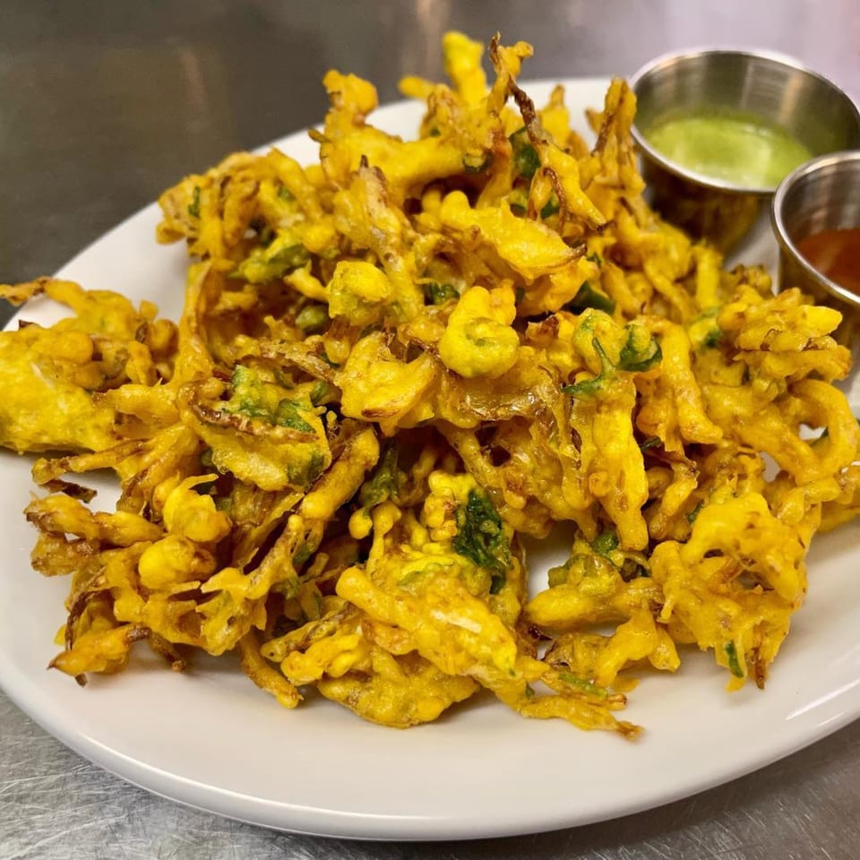 A plate of golden-fried Indian pakora, with green and red dipping sauces in metal cups.