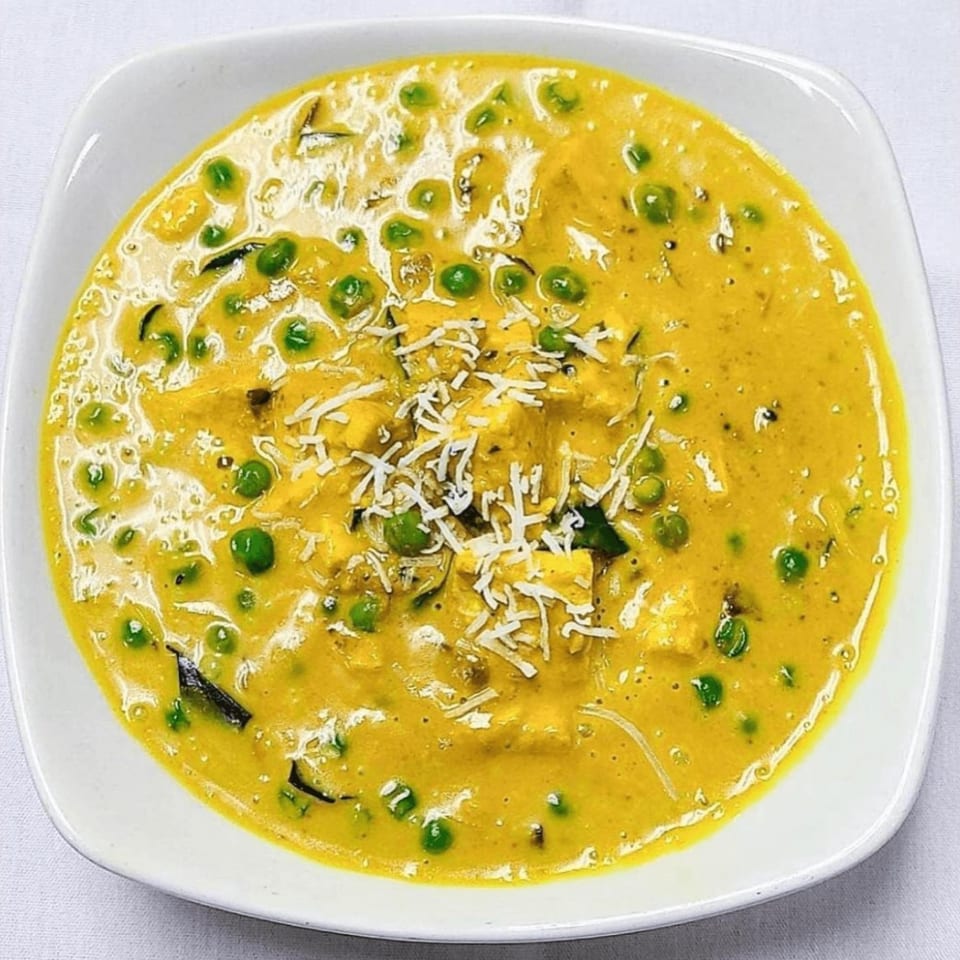A bowl of Gorkha Palace Indian Cuisine's yellow curry with green peas and paneer, topped with shredded cheese.