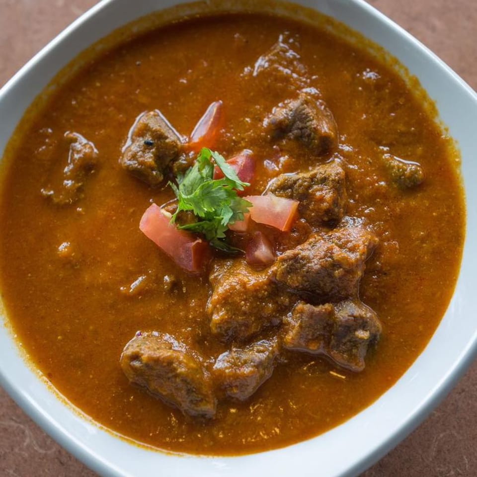 Gorkha Palace Indian Cuisine's rich, brown curry with meat chunks, garnished with fresh tomatoes and cilantro.