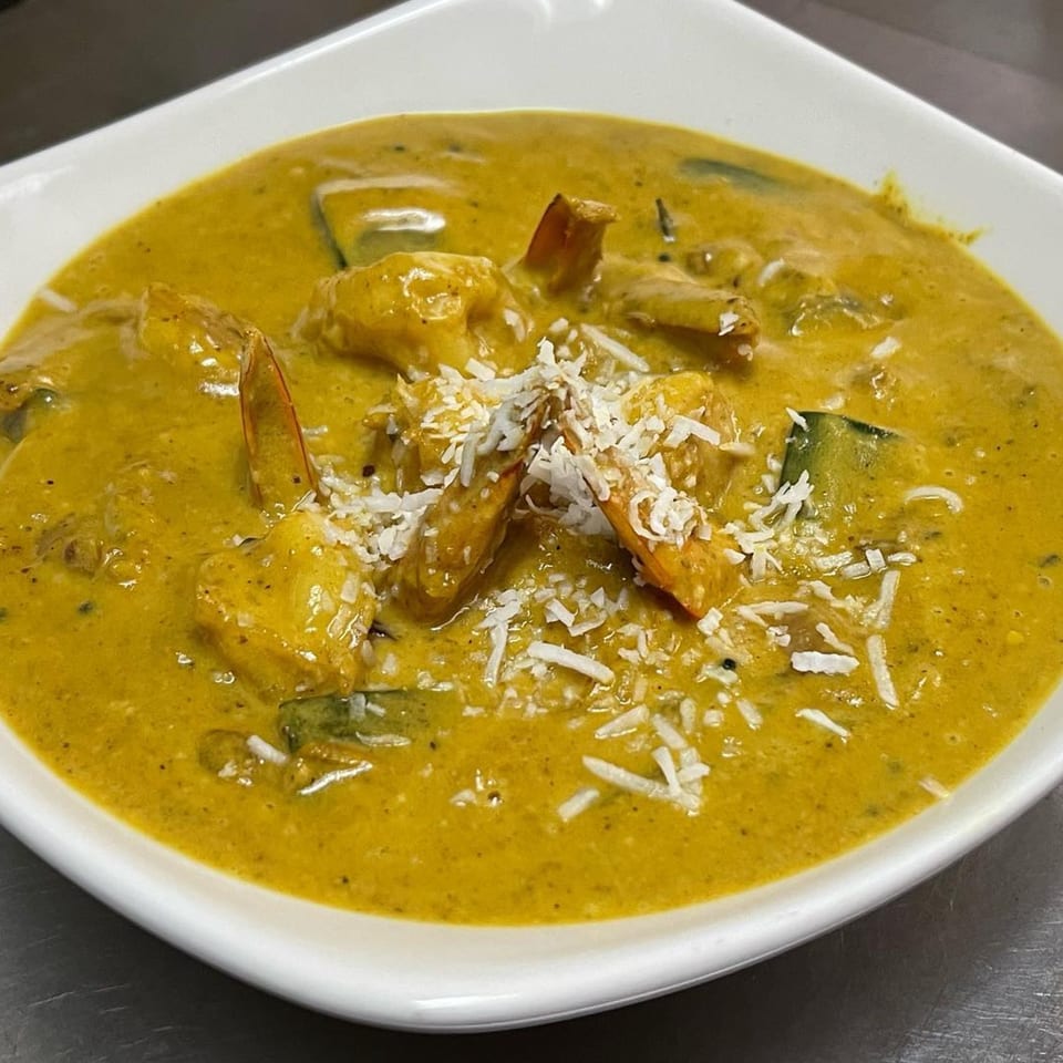 Indian shrimp curry with a rich yellow sauce, garnished with shredded coconut in a white bowl.