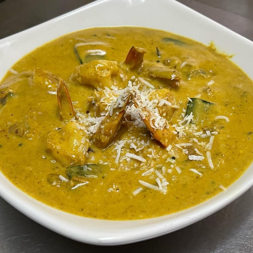 Indian shrimp curry with a rich yellow sauce, garnished with shredded coconut in a white bowl.